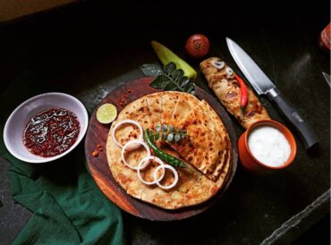 Golden, crispy aloo paratha, a traditional Indian flatbread stuffed with spiced mashed potatoes, served with a side of yogurt and pickles.