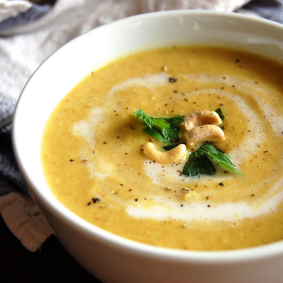 A warm bowl of creamy cauliflower soup garnished with a drizzle of olive oil, fresh herbs, and a sprinkle of black pepper, served in a rustic ceramic bowl on a wooden table