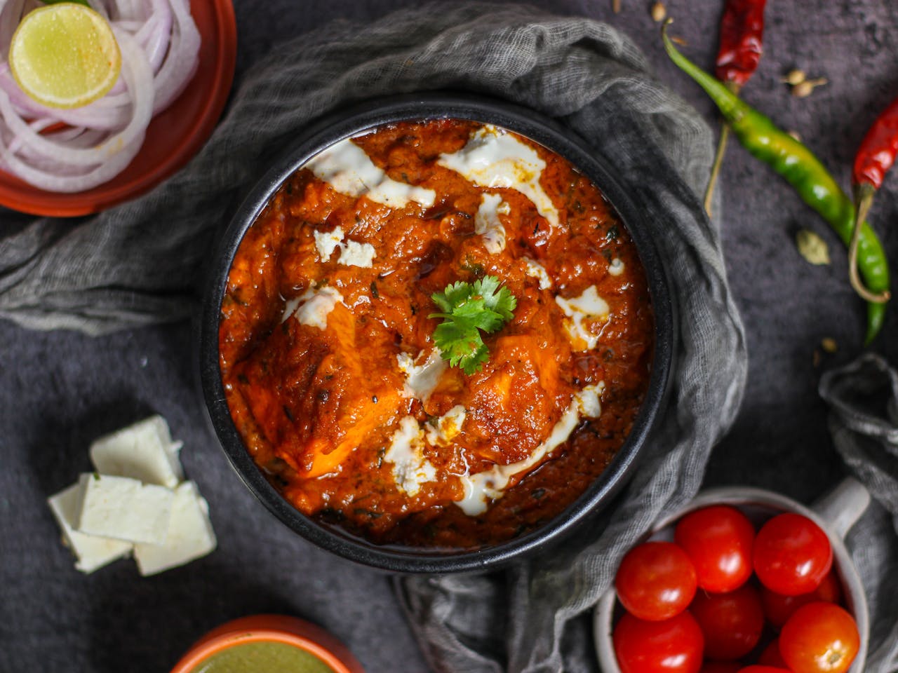A bowl of creamy Paneer Makhani, featuring soft paneer cubes in a rich, buttery tomato-based gravy, garnished with fresh cream and coriander leaves, served with naan and rice on the side