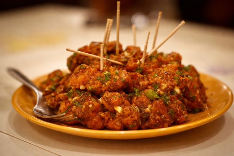 Plate of gobi manchurian with crispy cauliflower pieces in spicy sauce served with toothpicks.