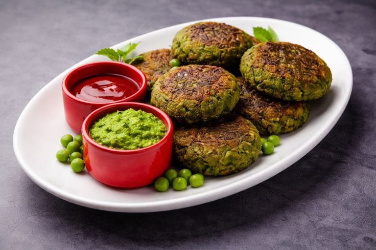 Hara bhara kababs served on a white plate with mint chutney and tomato sauce, garnished with green peas.