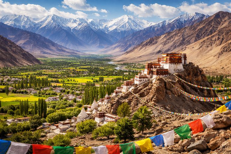 Buddhist monastery in Ladakh with colorful prayer flags and snow-capped Himalayan mountains in the background.