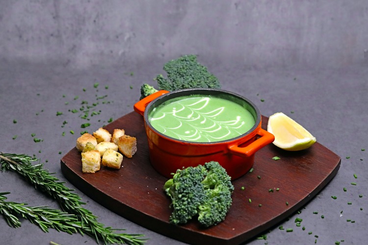 Creamy broccoli soup served in a bowl, garnished with a sprinkle of fresh herbs and a drizzle of cream, with a rich green color and a smooth texture.