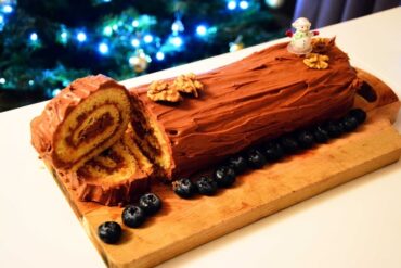 Decorated Christmas Yule Log with festive icing, holly, and powdered sugar, perfect for the holiday season.