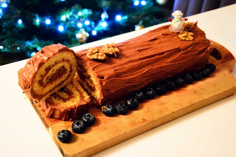 Decorated Christmas Yule Log with festive icing, holly, and powdered sugar, perfect for the holiday season.