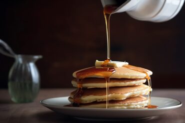 Stack of fluffy buttermilk pancakes topped with a pat of butter, drizzled with maple syrup, and garnished with fresh berries.