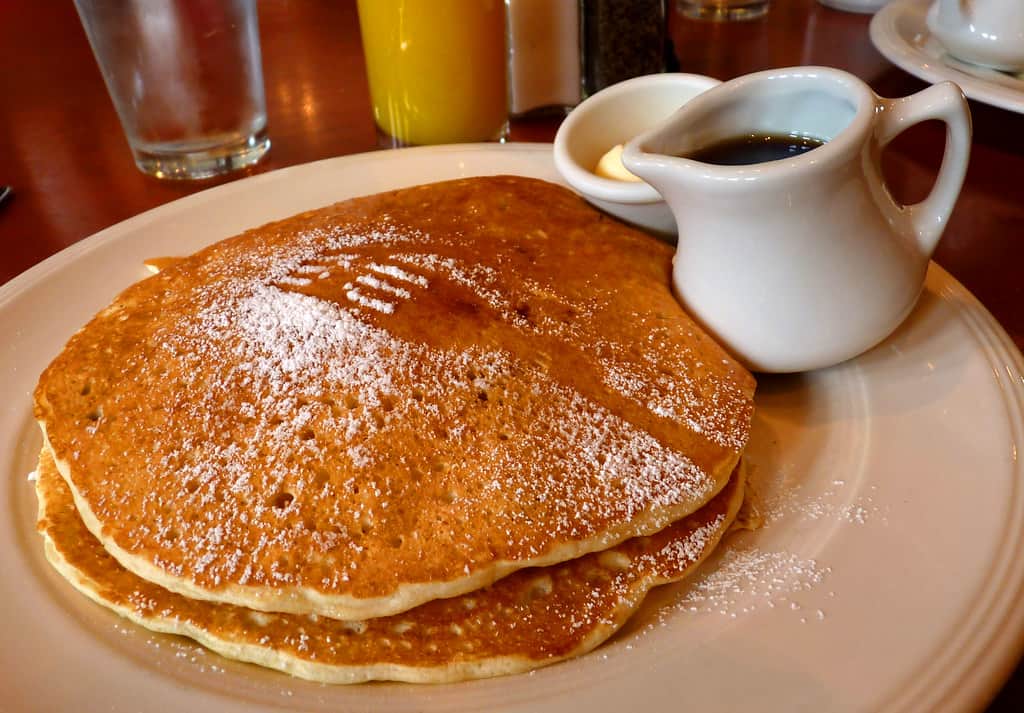 Golden, fluffy buttermilk pancakes stacked high, topped with a dollop of butter, a drizzle of maple syrup, and fresh fruit like berries.