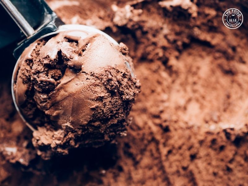 A scoop of rich, creamy chocolate ice cream in a cone, topped with chocolate shavings.