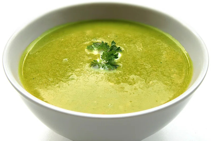 A bowl of creamy broccoli soup, smooth and velvety, with vibrant green color, garnished with a swirl of cream and a sprinkle of fresh herbs.