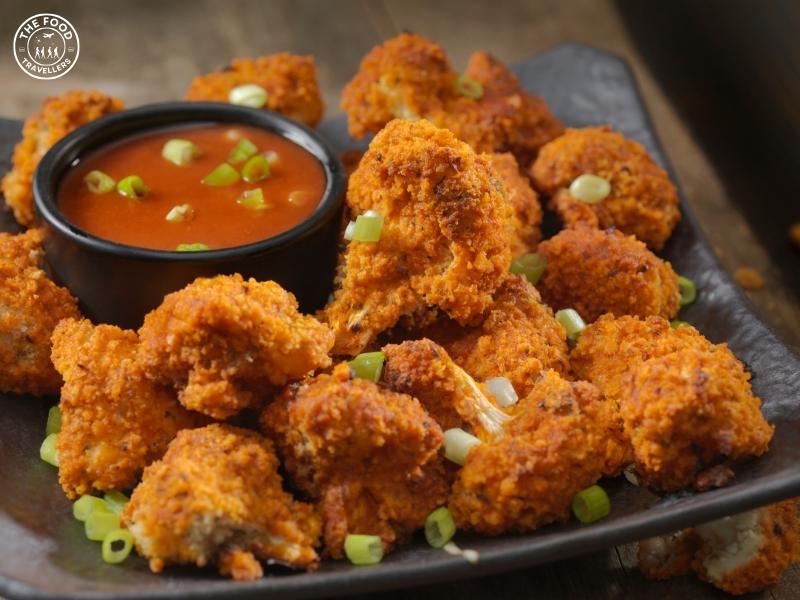 Crispy, golden-brown cauliflower pieces coated in a rich, spicy gochujang sauce, topped with sesame seeds and fresh green onions for added flavor and texture.