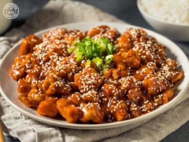 Golden, crispy cauliflower florets glazed with a spicy and savory gochujang sauce, garnished with sesame seeds and fresh herbs for a flavorful and vibrant dish.