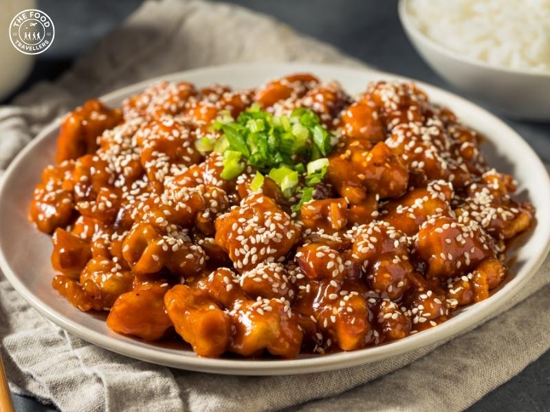 Golden, crispy cauliflower florets glazed with a spicy and savory gochujang sauce, garnished with sesame seeds and fresh herbs for a flavorful and vibrant dish.