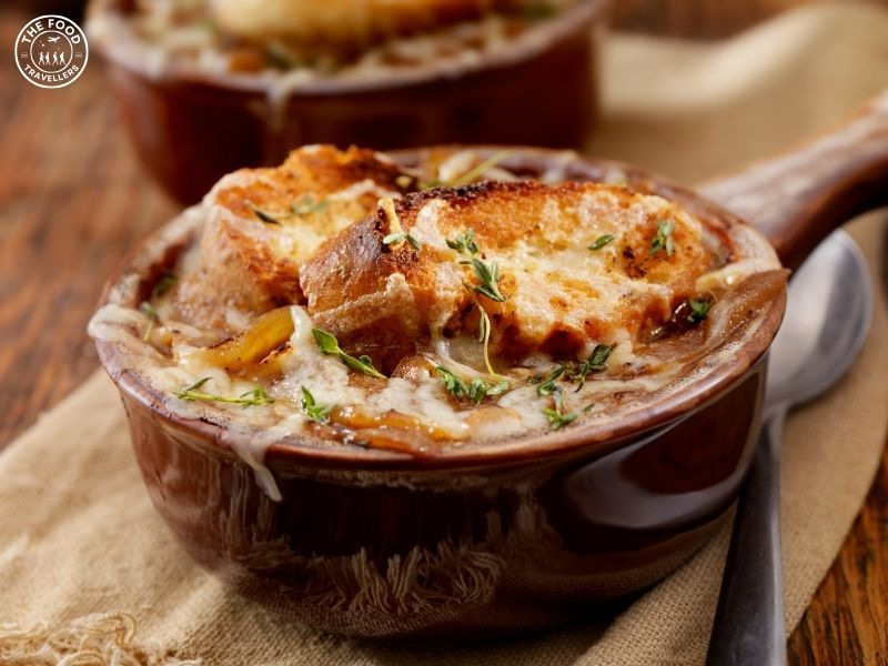 Vegetarian French onion soup topped with melted cheese and served in a rustic bowl, garnished with fresh herbs.