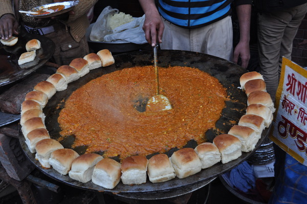 Authentic Mumbai Pav Bhaji served with a spicy vegetable mash, topped with chopped onions, fresh cilantro, and a slice of lemon, accompanied by buttery pav (bread rolls).