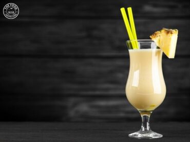 A refreshing Piña Colada cocktail served with a pineapple slice and cherry, garnished with a paper umbrella, set against a tropical backdrop.