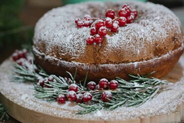 A freshly baked Christmas plum cake garnished with dried fruits and nuts, placed on a festive table setting.