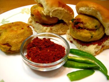 Delicious Vada Pav with crispy potato fritter and soft pav, served with chutneys and green chili.
