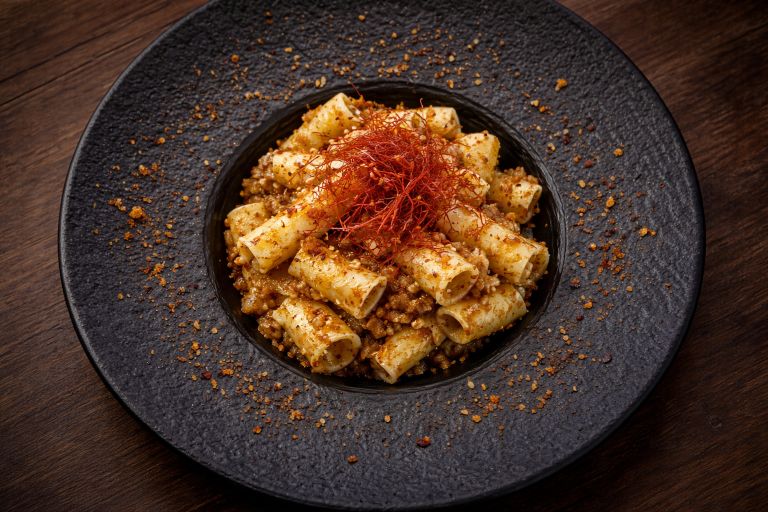 Creamy rigatoni pasta served on a black restaurant plate with parmesan and herbs