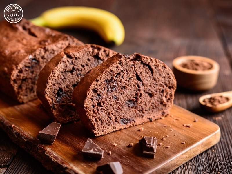 A slice of Veg Banana Bread with a moist, fluffy texture, topped with chocolate and served on a wooden plate.
