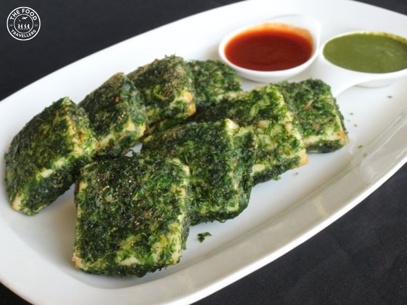 "Close-up of Chimichurri Paneer Tikka pieces on a sizzling hot plate, with vibrant green chimichurri sauce.