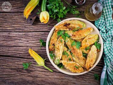 Golden, crispy fried zucchini flowers stuffed with a savory veggie filling, garnished and ready to enjoy.