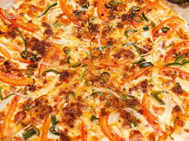 Close-up of Mexican Green Wave Pizza showcasing the vibrant green sauce, fresh toppings, and spicy details.