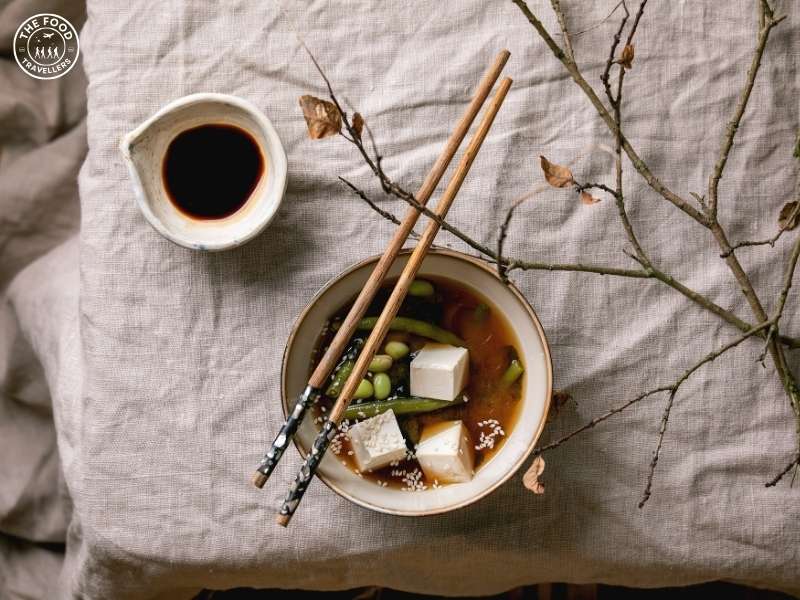 A bowl of vegetarian miso and tofu soup with a savory miso broth, soft tofu cubes, and colorful vegetables, garnished with green onions.