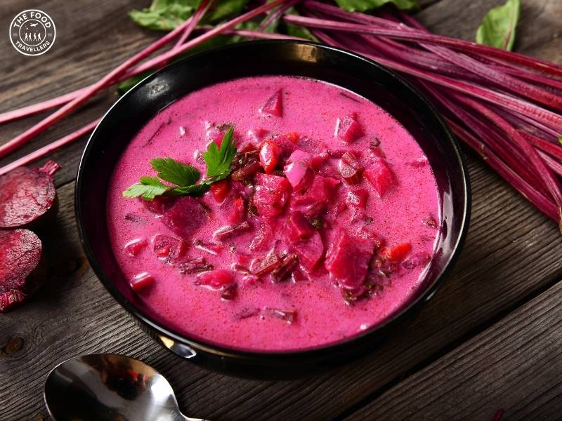 Bowls of creamy vegetarian pumpkin beetroot soup garnished with fresh herbs, showcasing vibrant orange and purple colors.
