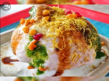 Raj Kachori: A crispy, golden sphere filled with yogurt, tangy chutneys, and spices, garnished with fresh herbs.