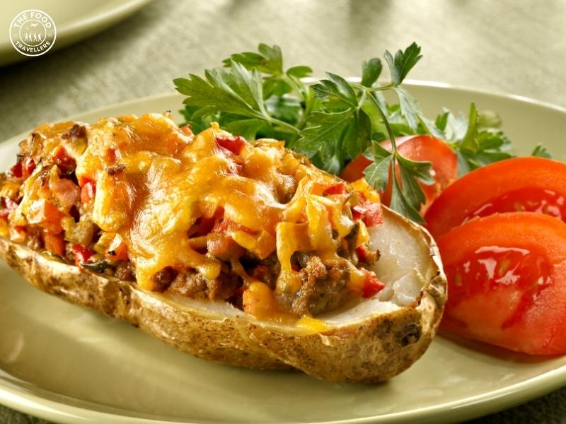 A variety of baked potatoes topped with cheese, broccoli, black beans, salsa, spinach, mushrooms, and sour cream, offering diverse flavors.