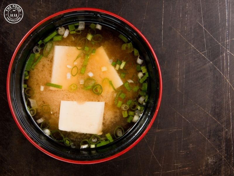 A bowl of Vegetarian Miso and Tofu Soup with rich miso broth, tender tofu cubes, and fresh vegetables, garnished with green onions.