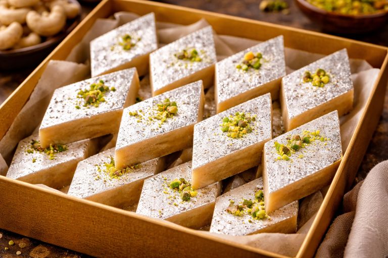 Box of kaju katli Indian cashew sweet topped with silver varak and pistachios