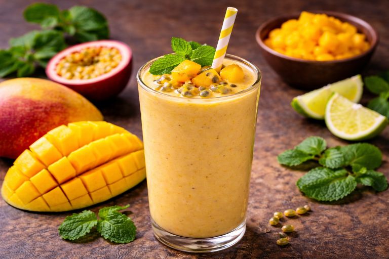 Mango passion fruit smoothie in a tall glass topped with fresh mango, passion fruit seeds, and mint