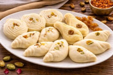Assorted traditional Bengali sandesh sweets in different shapes with pistachio and raisin garnish