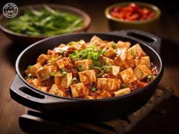 "A bowl of Vegan Mapo Tofu, featuring tender tofu in a rich, spicy sauce garnished with green onions and chili flakes.