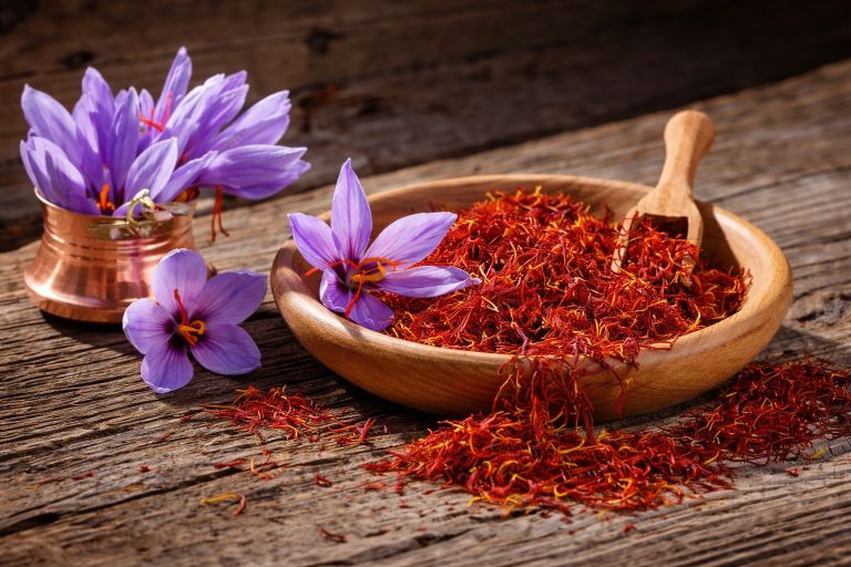 Kesar saffron threads in a wooden bowl with purple saffron flowers on a rustic wooden table