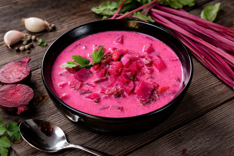 Pumpkin beetroot soup recipe served in a bowl with fresh beetroot pieces and herbs on a rustic wooden table