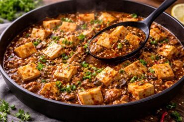 Vegan Mapo Tofu with soft tofu cubes in spicy Sichuan sauce garnished with scallions and sesame seeds.