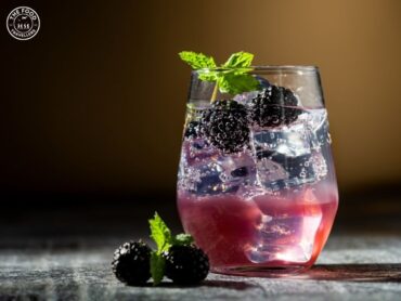 Close-up of a vibrant Blueberry-Ginger Fizz Mocktail in a glass, garnished with fresh blueberries, mint leaves, and a slice of ginger.
