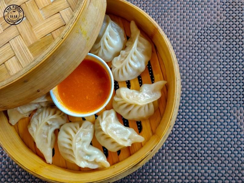 Steamed Veg Momos served on a plate with dipping sauce, showcasing a bite-sized vegetarian filling inside soft, doughy wrappers