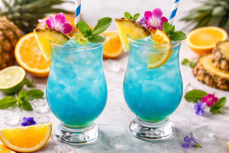 Tropical Mermaid Breezer Mocktail with pineapple, orange slice, mint, and edible flowers