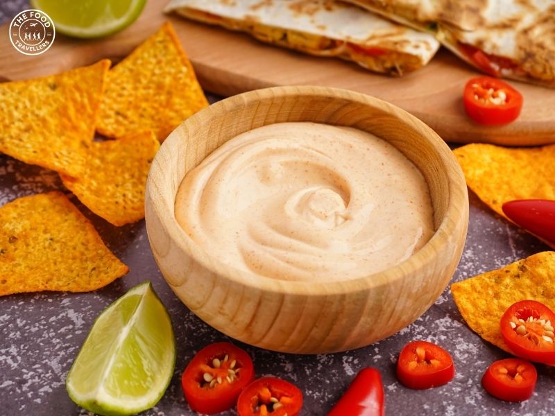 Homemade chipotle sauce in a bowl with chipotle peppers, nachos, lime on the side.