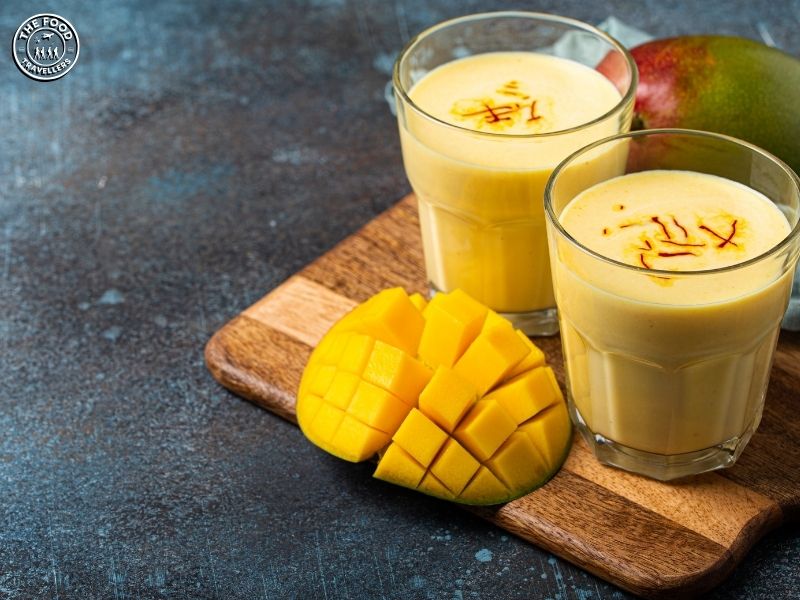 Chilled mango lassi in a glass, garnished with mint and cardamom.