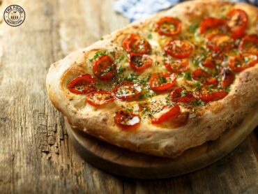 Freshly baked veg focaccia bread with cherry tomatoes, bell peppers, red onions, and rosemary on top.