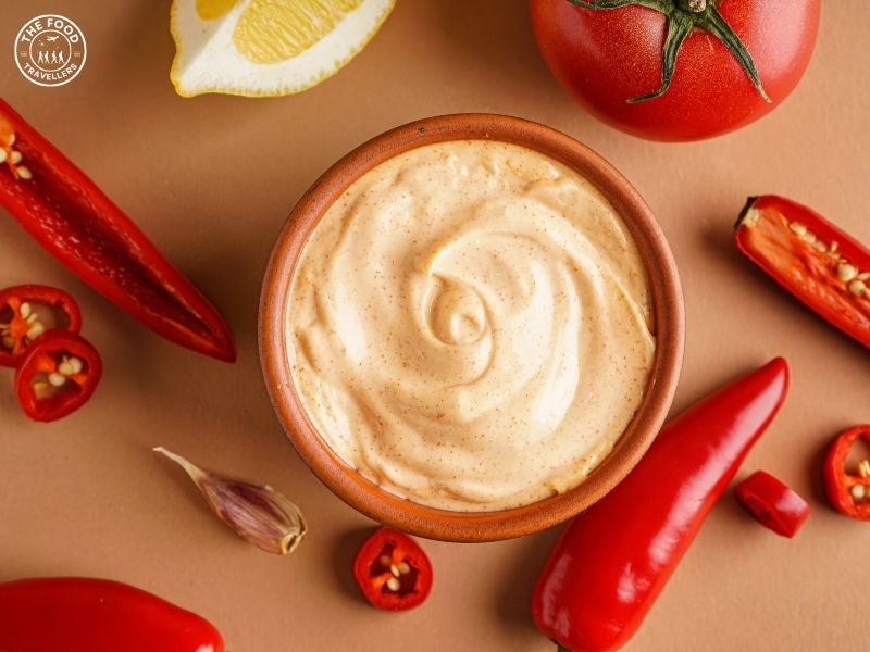 Creamy homemade chipotle sauce in a bowl surrounded by red chilies, lemon, and garlic on a neutral background
