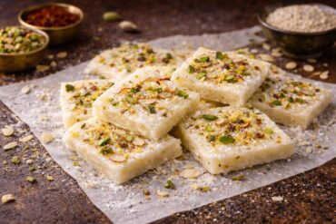 Traditional ice halwa squares topped with pistachios, almonds and saffron on a brass plate