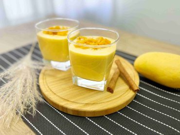 Chilled mango lassi garnished with mint, saffron and pistachios served in tall glasses