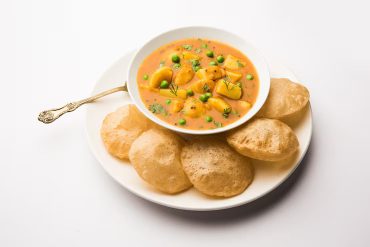 Luchi Aloo Dum recipe served with fluffy luchis and spicy Bengali potato curry on rustic wooden table