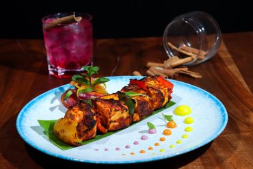 Sizzling chimichurri paneer tikka skewers with grilled bell peppers and onions on a cast iron platter.