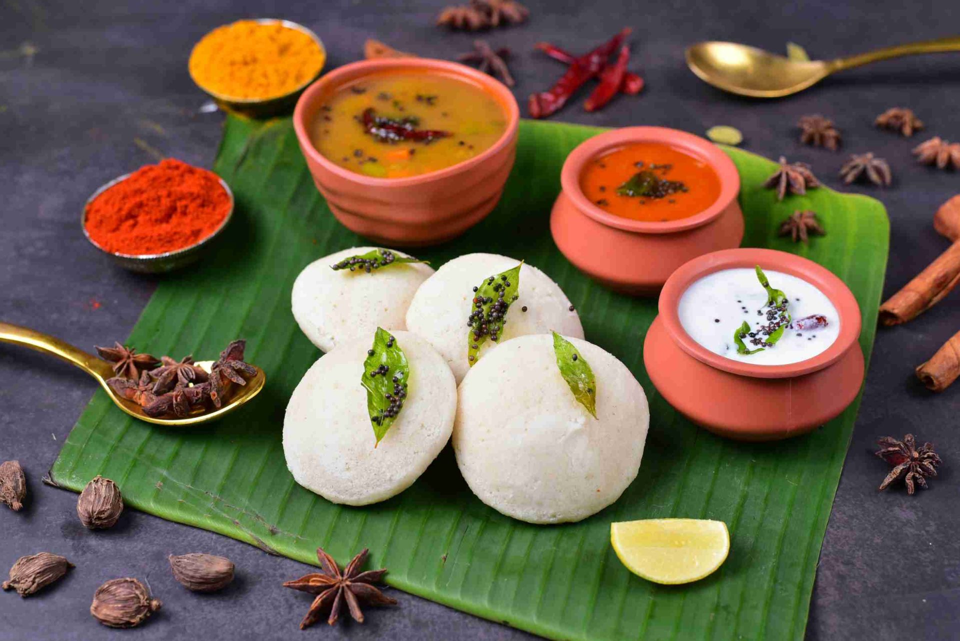 Idli recipe variations featuring steamed idli, thatte idli, podi idli, sambar idli, and mini button idli on rustic table